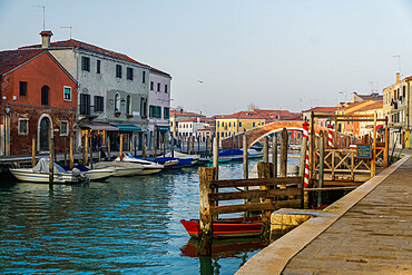 View of Ponte San Martino stone bridge over canal with colorful buildings and moored boats on wooden wharf pilings, Murano, Venice, UNESCO World Heritage Site, Veneto, Italy, Europe