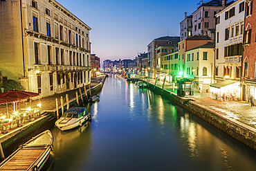 Evening canal view of low rise traditional buildings and wooden wharf pilings with moored boats, Venice, UNESCO World Heritage Site, Veneto, Italy, Europe