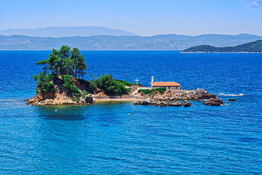 Small Christian church stone-built chapel with a cross on a small island strip in calm sea, Greek Islands, Greece, Europe