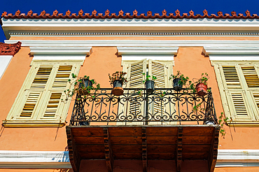 Low-angle view of a traditional house with closed wooden shutters and a balcony with plant pots against a blue sky in Nafplion, Peloponnese, Greece, Europe