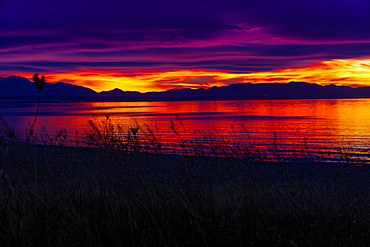 Mediterranean sunset over calm sea, orange and purple clouds over mountainous landscape silhouette, Greece, Europe