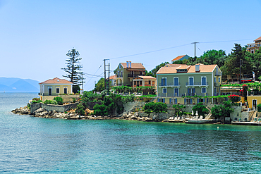 Fiscardo village of low rise houses with red tiled rooftops by a beach with bathers, Fiscardo, Kefalonia, Ionian Island, Greek Islands, Greece, Europe