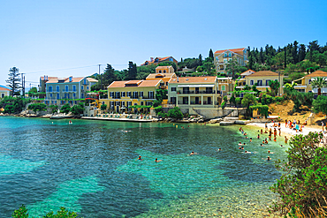 Fiscardo village of low rise houses with red tiles rooftops by a beach with bathers, Fiscardo, Kefalonia, Ionian Island, Greek Islands, Greece, Europe