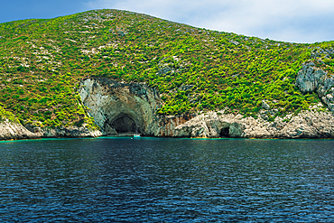 Moored yacht outside cave formation on a rocky hill with green plantation stretching to the sea, Zakynthos, Ionian Islands, Greek Islands, Greece, Europe