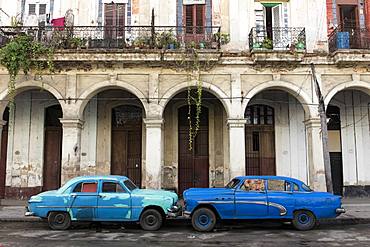 Two blue cars face nose to nose outside a dilapidated building, Havana, Cuba, West Indies, Caribbean, Central America