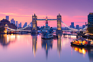 Sunrise view of HMS Belfast and Tower Bridge reflected in River Thames, with Canary Wharf in background, London, England, United Kingdom, Europe