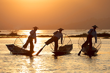 Three fishermen row with one leg at sunset on Inle Lake, Shan State, Myanmar (Burma), Asia