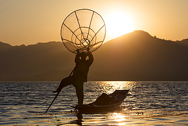 A fisherman standing on one leg and holding his fishing net at sunset on Inle Lake, Shan State, Myanmar (Burma), Asia