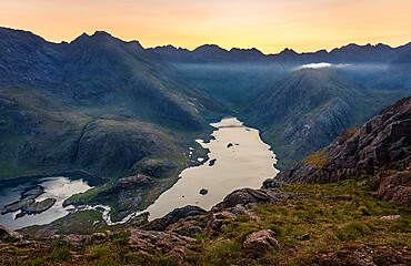 The sun setting behind the Black Cuillin Ridge with the remote Loch Coruisk in the glen below, Isle of Skye, Inner Hebrides, Scotland, United Kingdom, Europe