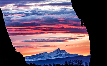 A rock climber scales a wall while the sun sets over a mountain in the distance, United States of America, North America