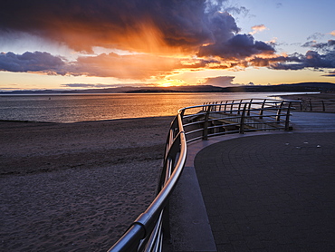 Under dramatic coloured clouds, the sun sets in line with railings on the slipway at the RNLI station, Exmouth, Devon, England, United Kingdom, Europe