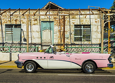 A classic American car driving past an old building in Varadero, Cuba, West Indies, Caribbean, Central America