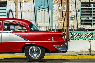 A classic American car driving past an old building in Varadero, Cuba, West Indies, Caribbean, Central America