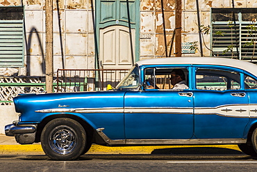 A classic American car driving past an old building in Varadero, Cuba, West Indies, Caribbean, Central America