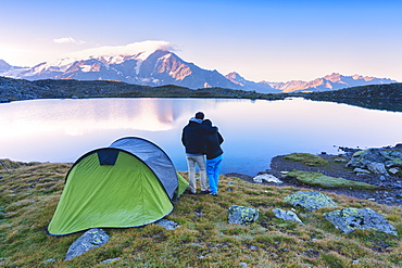 A couple admires the sunrise at the lake of Manzina, Valfurava, Valtellina, Italy, Europe