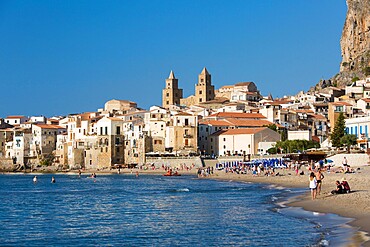 View from beach along water's edge to the town and UNESCO World Heritage Site listed Arab-Norman cathedral, Cefalu, Palermo, Sicily, Italy, Mediterranean, Europe