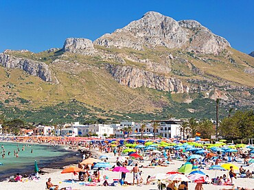 View across colourful crowded beach to the rugged slopes of Pizzo di Sella, San Vito Lo Capo, Trapani, Sicily, Italy, Mediterranean, Europe