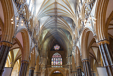 View along sunlit nave to the colourful stained glass Great West Window of Lincoln Cathedral, Lincoln, Lincolnshire, England, United Kingdom, Europe