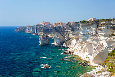 View over rocky cove along rugged limestone cliffs to the distant citadel, Bonifacio, Corse-du-Sud, Corsica, France, Mediterranean, Europe