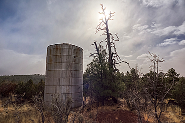 An old water tank perched on a cliff overlooking the T-Bar Ranch Homestead in the Coconino National Forest of Arizona. The white specks in the image are snow flakes from an approaching snow storm. Ranch is abandoned and owned by National Forest Service.