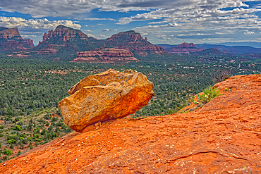 A boulder balanced on the edge of a cliff in Sedona with the Twin Buttes and Cathedral Rock in the distance, Arizona, United States of America, North America