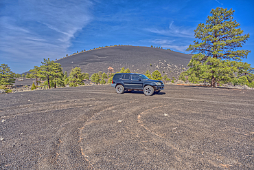 An SUV traveling near Volcanic cinder hills in Coconino National Forest near Sunset Crater National Monument of Arizona.