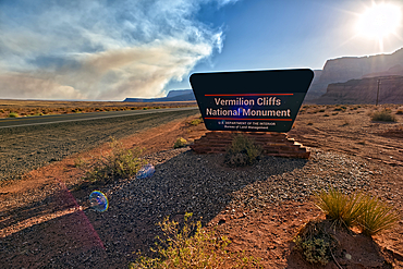 Sign for Vermilion Cliffs National Monument Arizona near sunset with smoke in the sky from the Dragon Bravo Wildfire burning on North Rim.