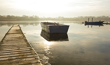 A rowing boat floats adrift on a frozen lake beside an empty walkway at Hornsea Mere, East Yorkshire, Yorkshire, England, United Kingdom, Europe