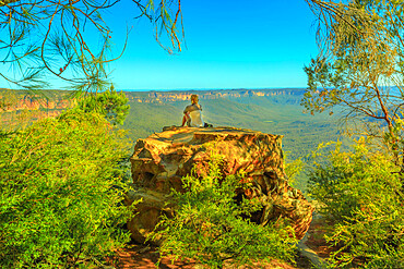 Tourist woman relaxing after hiking and enjoying panoramic views of granite boulders rock formations from Baltzer Lookout in Blue Mountains National Park near Sydney, New South Wales, Australia, Pacific