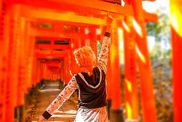 Woman walking beneath red torii gates at Fushimi Inari Shinto shrine, Kyoto, Japan, Asia