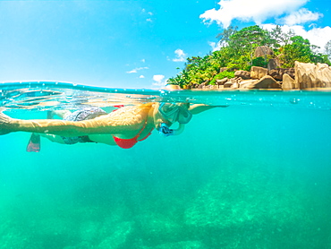 Split view of female tourist snorkelling underwater and landscape of St. Pierre Island coral reef, Seychelles, Indian Ocean, Africa