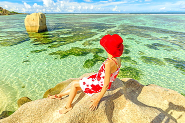 Tourist woman in red hat on a granite boulder at Anse Source d'Argent, La Digue Island, Seychelles, Indian Ocean, Africa