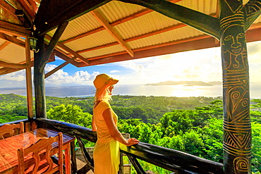 Tourist woman in yellow dress looks towards Praslin Island and La Digue panorama from highest point of island at sunset, La Digue, Seychelles, Indian Ocean, Africa