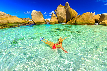 Happy woman in bikini lying in turquoise water in the natural pool of Seychelles beach, Anse Marron, La Digue, Seychelles, Indian Ocean, Africa