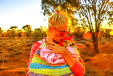 Tourist woman holding and kissing kangaroo joey at sunset light in Australian Outback, Red Center, Northern Territory, Australia, Pacific