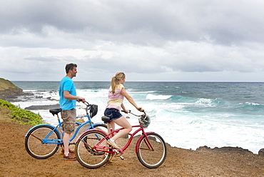 Couple on bikes looking out at the ocean on the shores of Kauai, near Kapaa, Kauai, Hawaii, United States of America, North America