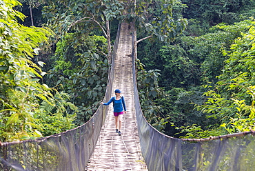 A woman crosses a precarious looking suspension bridge over the jungle in Laos, Indochina, Southeast Asia, Asia