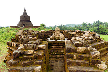 A ruined stone stupa with damaged Buddha statue in the centre, with West Myatazaung Pagoda in the background, Mrauk U, Rakhine, Myanmar (Burma), Asia