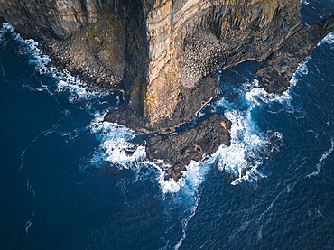 Aerial view of the rugged coastline of the Faroe Islands, showcasing towering sea cliffs that plunge into the deep blue ocean.