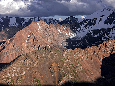 Stunning mountainous landscape of Kyrgyzstan illuminated by fading sunlight and shadowy clouds.