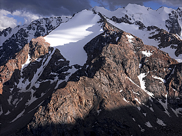 Stunning mountainous landscape of Kyrgyzstan illuminated by fading sunlight and shadowy clouds.