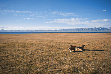 Relaxing view of wooden chairs near the tranquil waters of Song-Kol Lake, surrounded by vast grasslands and mountains, Kyrgyzstan, Central Asia, Asia