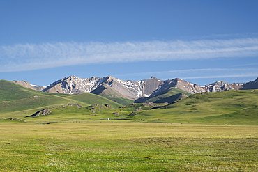 Vast green meadows meet majestic mountains at Song-Kol Lake in Kyrgyzstan under a clear blue sky