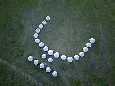 Line of white yurts in a curved pattern on grassy plain, viewed from above near Song Kol Lake, Kyrgyzstan