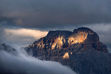 Sunset on Croda Rossa d'Ampezzo mountains surrounded by the fog and darkness with only a few spots of sun light, Dolomites, Veneto, Italy, Europe