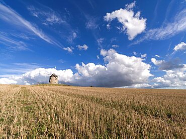 Windmill in a cropped field with a blue sky with white clouds, Normandy, France