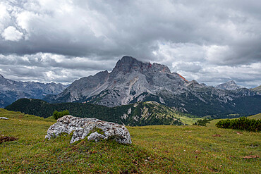 Panorama of the Croda Rossa D'ampezzo with pastures and a single rock in the foreground and a cloudy sky, Dolomites, Italy, Europe