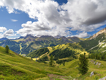 Mountain pastures on a sunny day with a white cloudy sky and light illuminating the mountain below, Dolomites, Italy, Europe