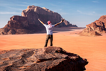 A man with a turban and his hands raised standing on a rock in the Wadi Rum desert