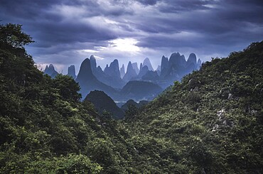 Yangshuo mountains with dark clouds framed by hills, Yangshuo, Guangxi, China, Asia